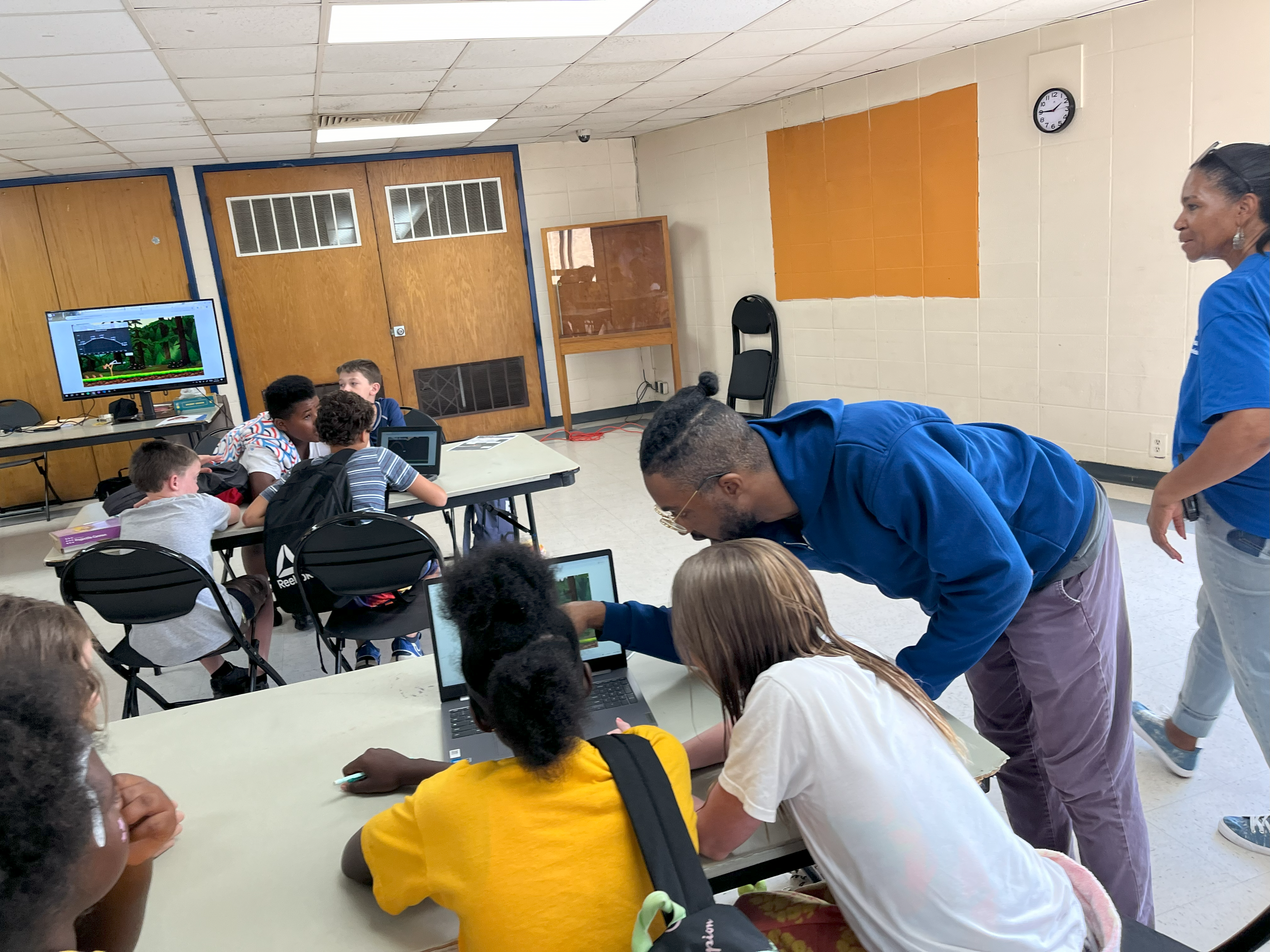 four summer camp students and a lab instructor huddled around a laptop with a science simulation